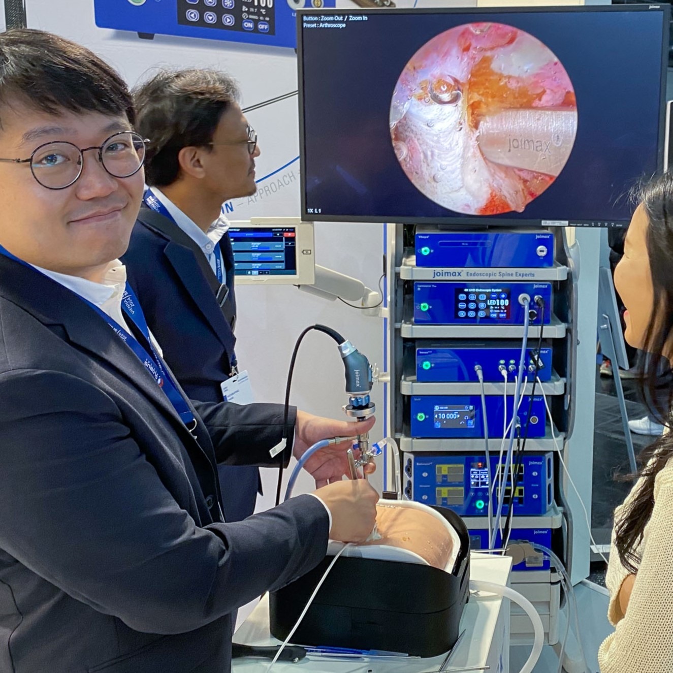 Surgeon shows endoscopic approach at a congress booth on an Upsurgeon lumbar spine model. The Navento tower by joimax is visible in the background
